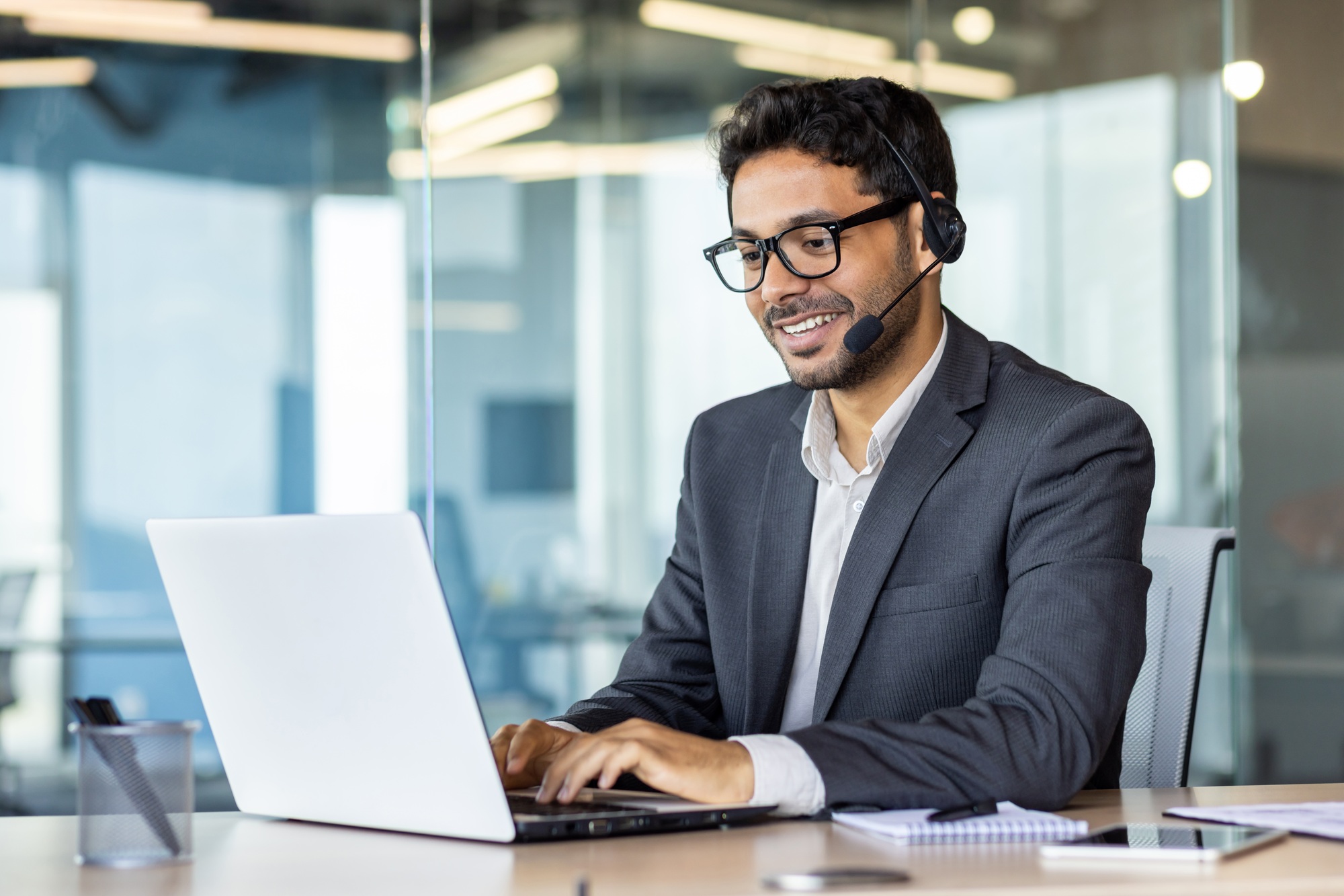 Young successful man at workplace with headset phone typing on laptop keyboard, customer support